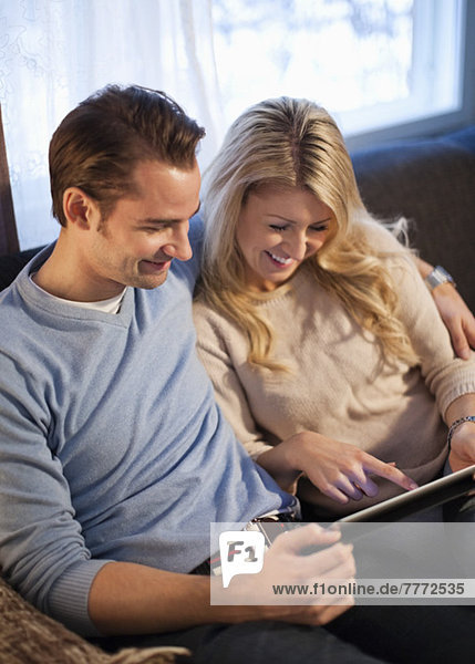 Glückliches Paar mit digitalem Tablett auf dem Sofa im Wohnzimmer