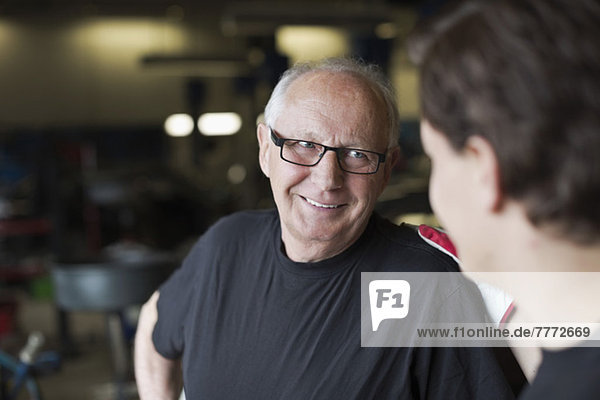 Happy senior male mechanic smiling at coworker in auto repair shop