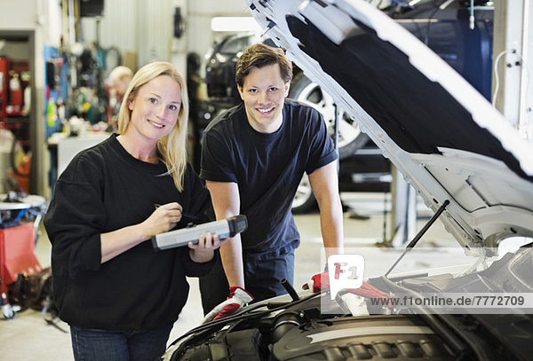 Portrait of happy mid adult female mechanic holding digital tablet standing with coworker by open car hood