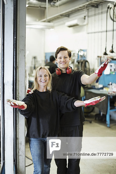 Porträt von glücklichen Mechanikern  die mit erhobenen Armen in der Werkstatt stehen.