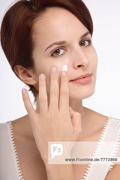 Portrait of a young brunette woman applying cream on right cheek