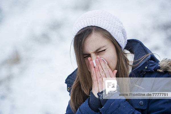 Junge Frau in Winterkleidung schnäuzt sich die Nase