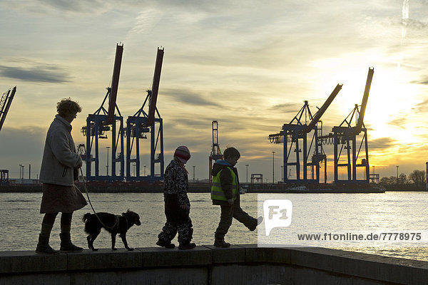 Woman with a dog and two children walking along a wall in front of gantry cranes  Container Terminal Burchardkai