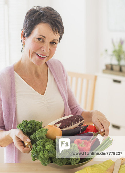 Portrait of mature woman holding wok with vegetables