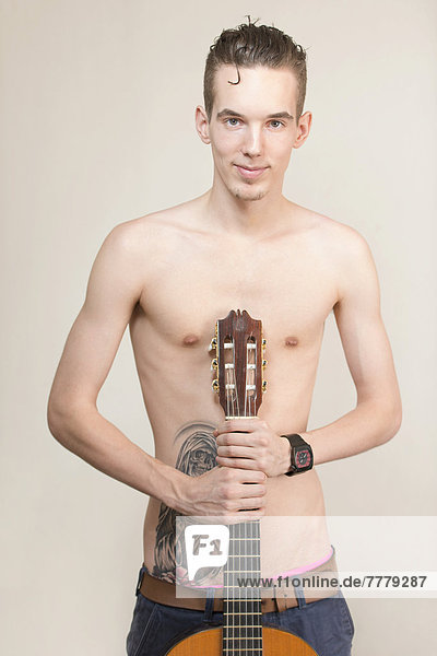 Junger Mann mit Tätowierung und nacktem Oberkörper hält eine Gitarre