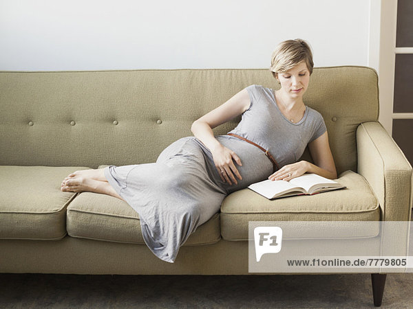 Pregnant woman lying on sofa reading