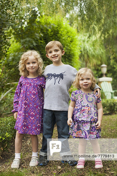 Brother (6-7) and sisters (2-3 4-5) posing together in garden