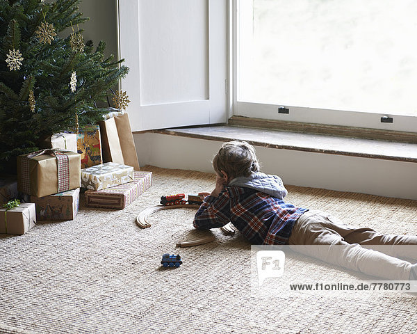 Junge spielt mit Zügen am Weihnachtsbaum