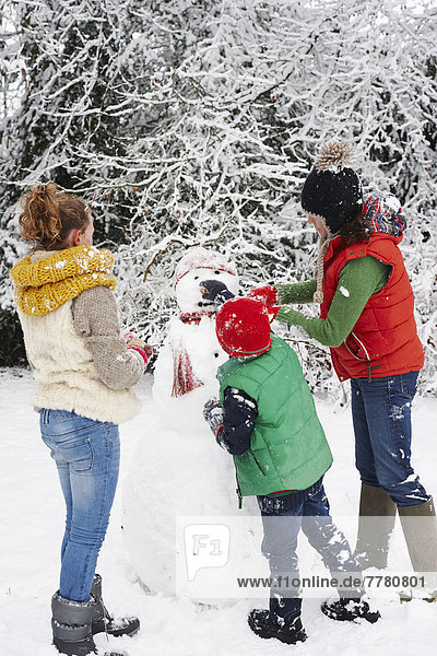 Mutter und Kinder machen Schneemann im Freien