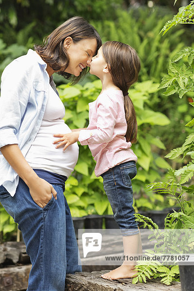Mädchen küsst schwangere Mutter im Freien