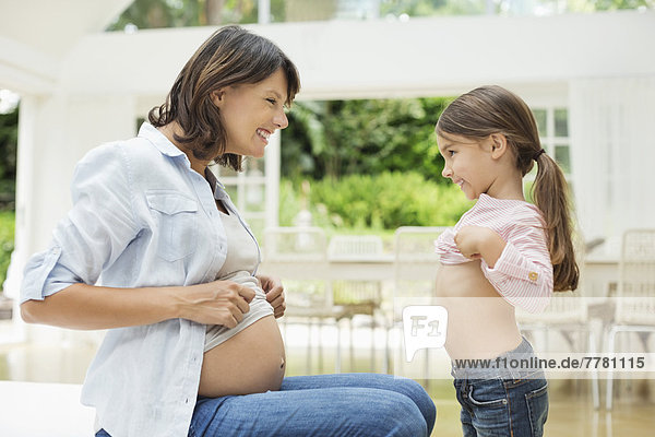 Mädchen und schwangere Mutter vergleichen Bäuche