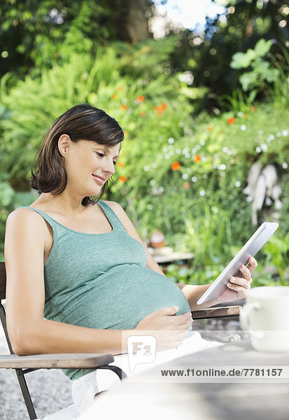 Schwangere Frau mit Tablet-Computer im Freien