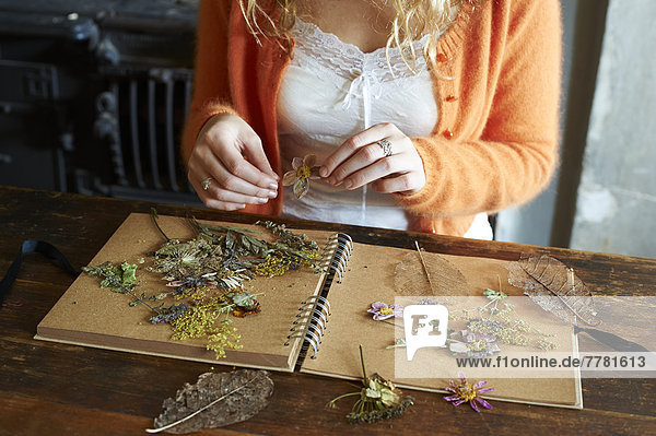 Frau arrangiert getrocknete Blumen und Kräuter auf Notizbuch