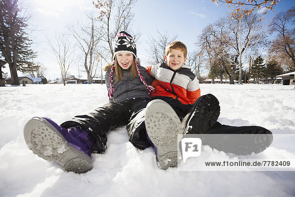 Caucasian children sitting in snow outdoors