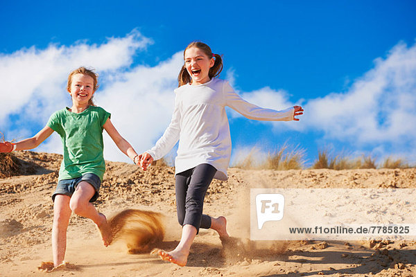 Zwei Mädchen rennen die Sanddüne hinunter.