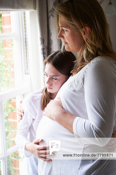 Schwangere Mutter mit jugendlicher Tochter  die durchs Fenster schaut.