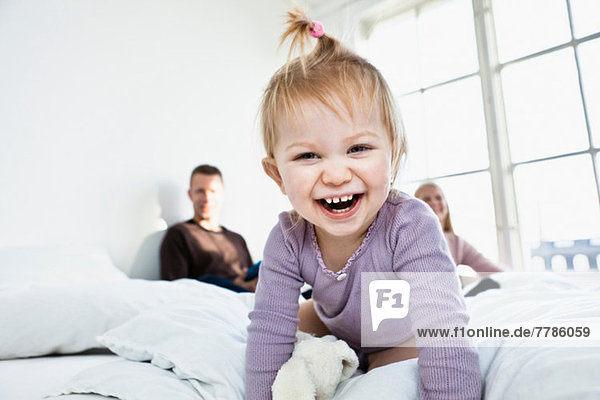 Kleinkind auf dem Bett der Eltern mit Blick auf die Kamera  lachend