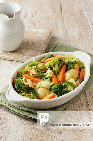 Gemüseauswahl bestehend aus Brokkoli  Karotten  neuen Kartoffeln und Kohl in weißer Servierplatte auf grünem Tuch