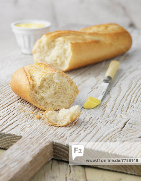 Weißes Baguette mit Butter auf weißem Holzbrett
