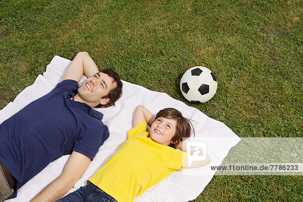 Vater und Sohn auf Decke liegend mit Fußball  hoher Winkel