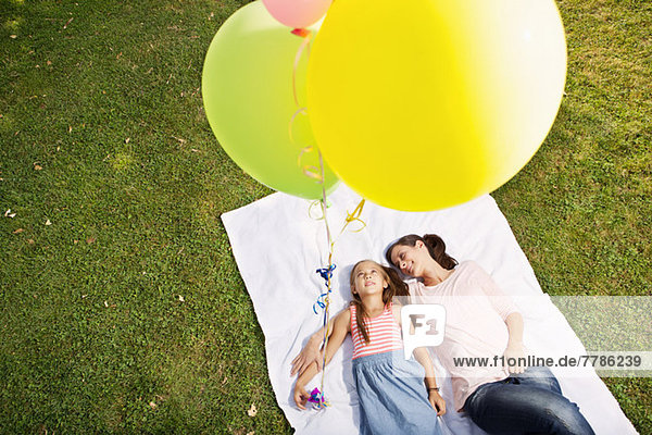 Mutter und Tochter liegen auf einer Decke und halten Luftballons  hoher Winkel