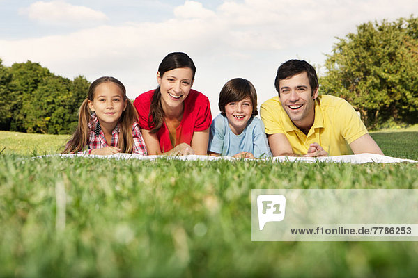 Porträt einer Familie mit zwei Kindern auf Gras liegend