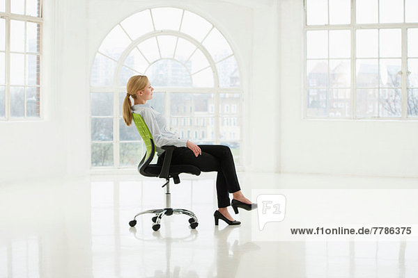 Geschäftsfrau sitzt auf einem Bürostuhl im kargen weißen Raum