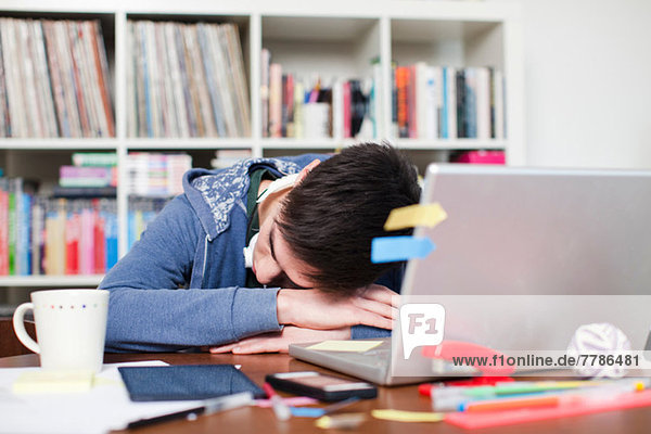 Männlicher Student schläft am Schreibtisch