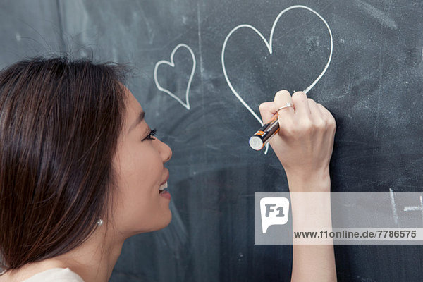 Junge Frau zeichnet Herz auf Tafel