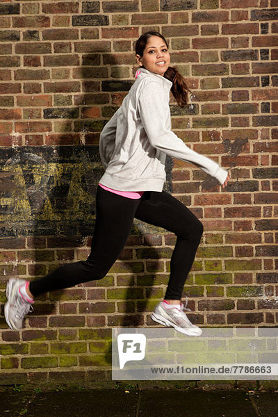 Junge Frau beim Springen an der Ziegelmauer