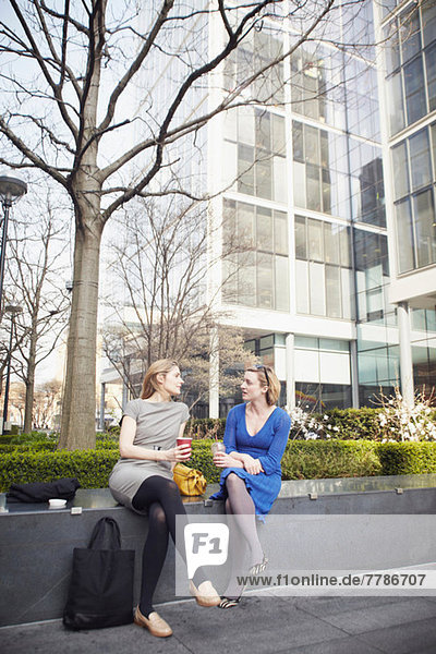 Businesswomen sitting on wall for coffee break