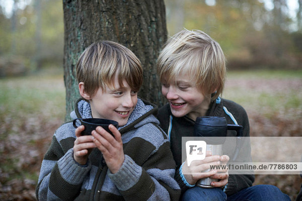 Boys drinking hot drinks in forest