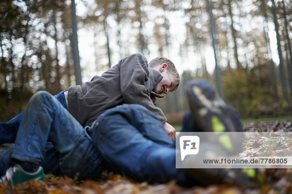 Boys play fighting on forest floor