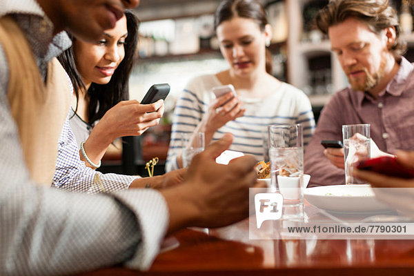 Friends at restaurant texting and showing photos using cell phones