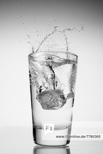 Eiswürfel  der in ein Glas Wasser fällt.