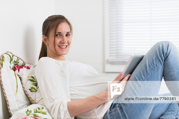Porträt einer schwangeren Frau auf dem Bett mit digitalem Tablett