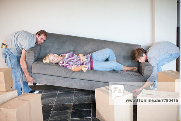 Young woman moving house on sofa being carried by men