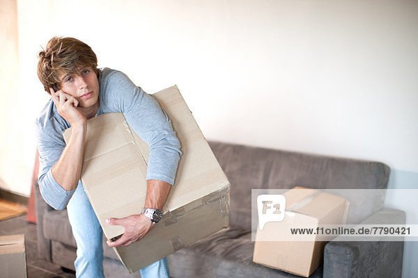 Young man moving house on cell phone carrying box