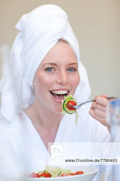 Young woman wearing towel on head eating salad