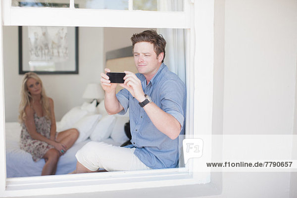 Young man taking photograph through window with smartphone