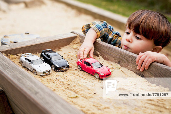 Männliches Kleinkind  das mit Spielzeugautos im Sandkasten spielt