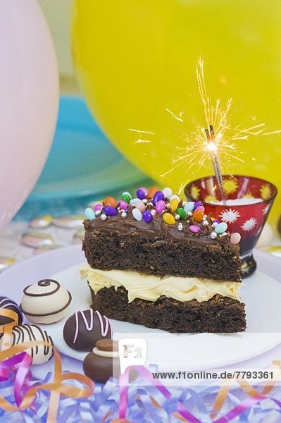 Ein Stück Schokoladenkuchen mit bunten Süssigkeiten für eine Party  Wunderkerze  Konfekt