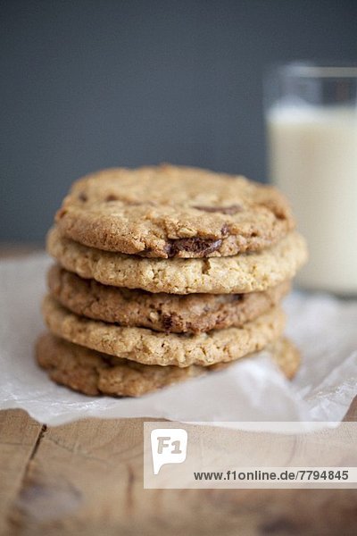 Chocolatechip Cookies mit Erdnussbutter und Haferflocken auf Backpapier vor einem Milchglas