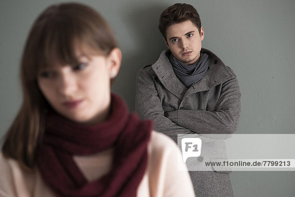 Portrait of Young Man Standing behind Young Woman  Looking at her Intensely  Studio Shot on Grey Background