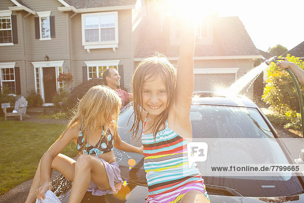 A family washes their car in the driveway of their home on a sunny summer afternoon in Portland  Oregon  USA