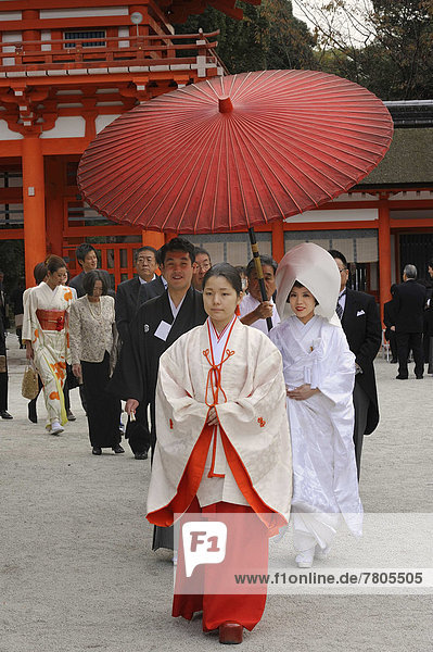 Japanese woman wearing scarlet hakama pants and a white kimono shirt with lengthy sleeves  in front of the gatehouse of Shimogamo Shrine