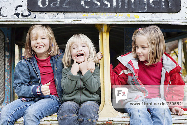 Drei Kinder sitzen in einem ausrangierten Bus