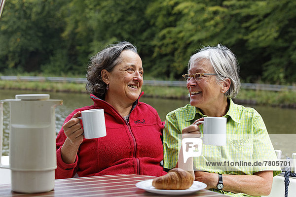 Zwei Urlauberinnen beim Frühstück auf der Heckterrasse einer Penichette Hausboot auf dem Canal des Vosges früher Canal de l?Est bei PK 101
