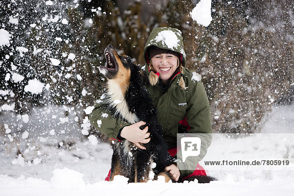 Young woman playing with an Australian Shepherd dog in the snow