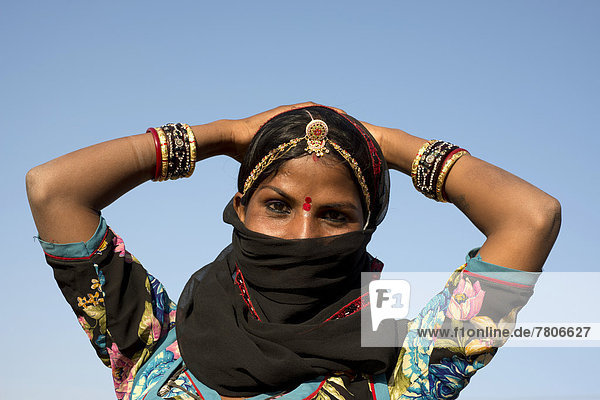 Young Indian woman with jewellery and a bindi covering her face with a black veil